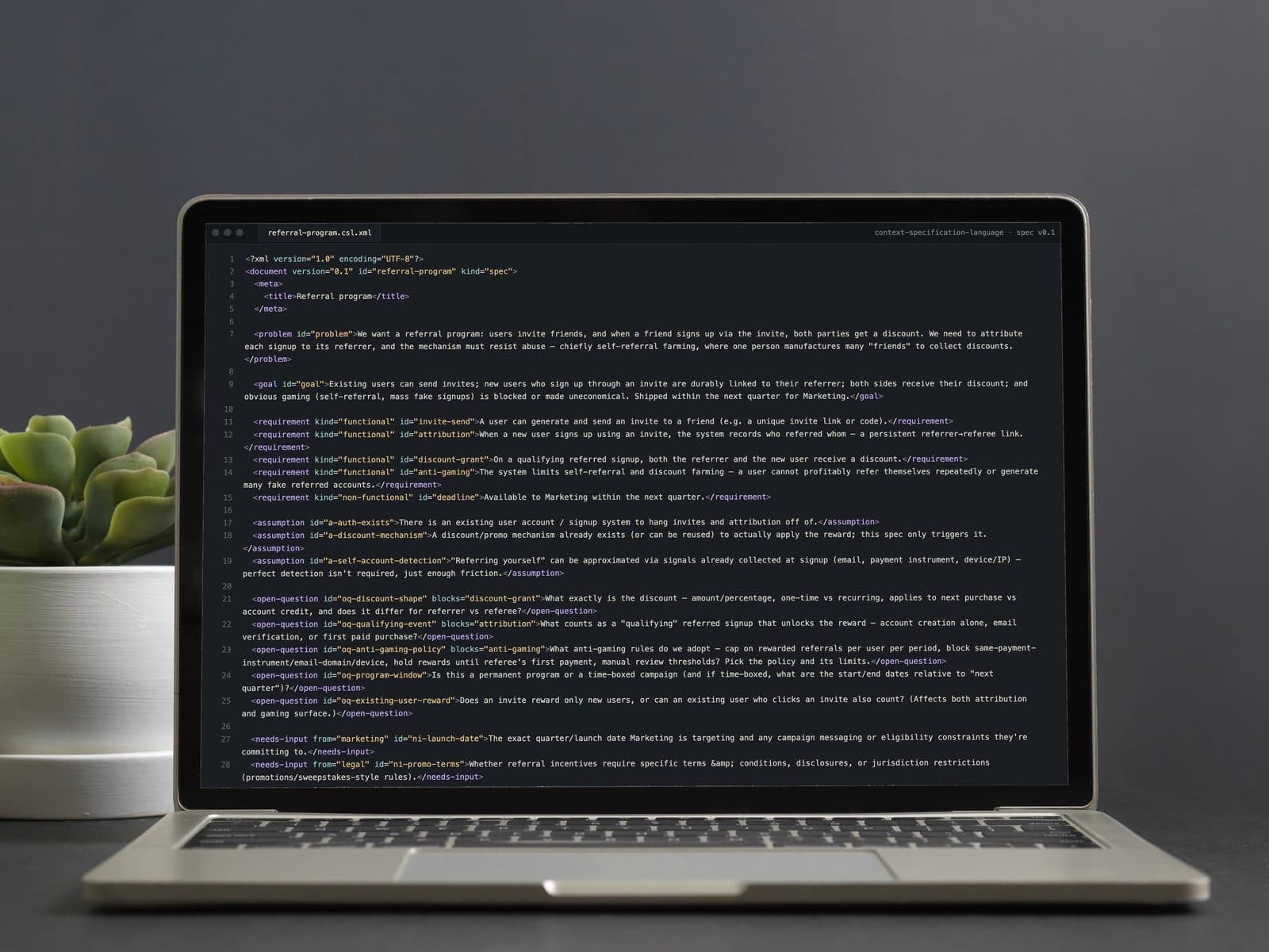 Un portátil sobre un escritorio cun ficheiro de especificación en Context Specification Language para un programa de referidos, aberto nun editor de código